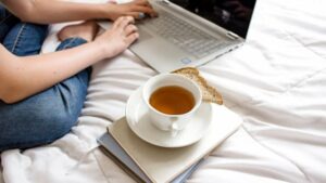 a woman sitting on the bed working on her computer with a cup of tea